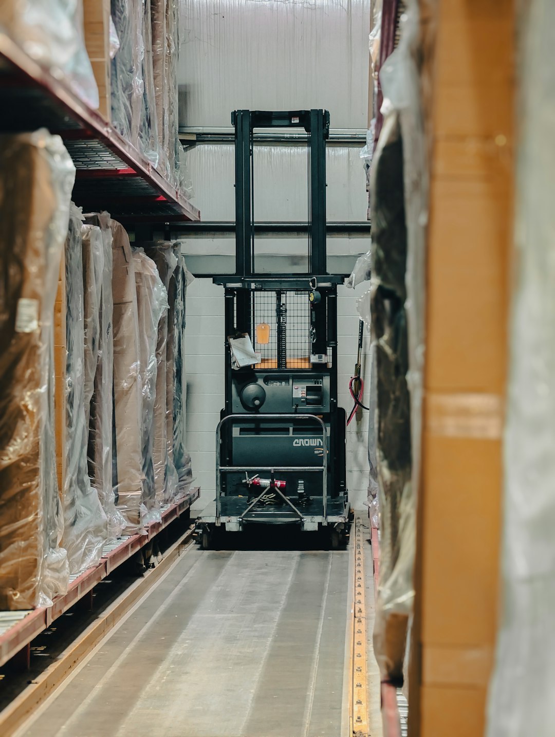 A lone forklift sits idle in a narrow warehouse aisle, surrounded by towering shelves packed with inventory. The scene evokes a sense of organized chaos, hinting at the bustling activity that takes place within these walls.